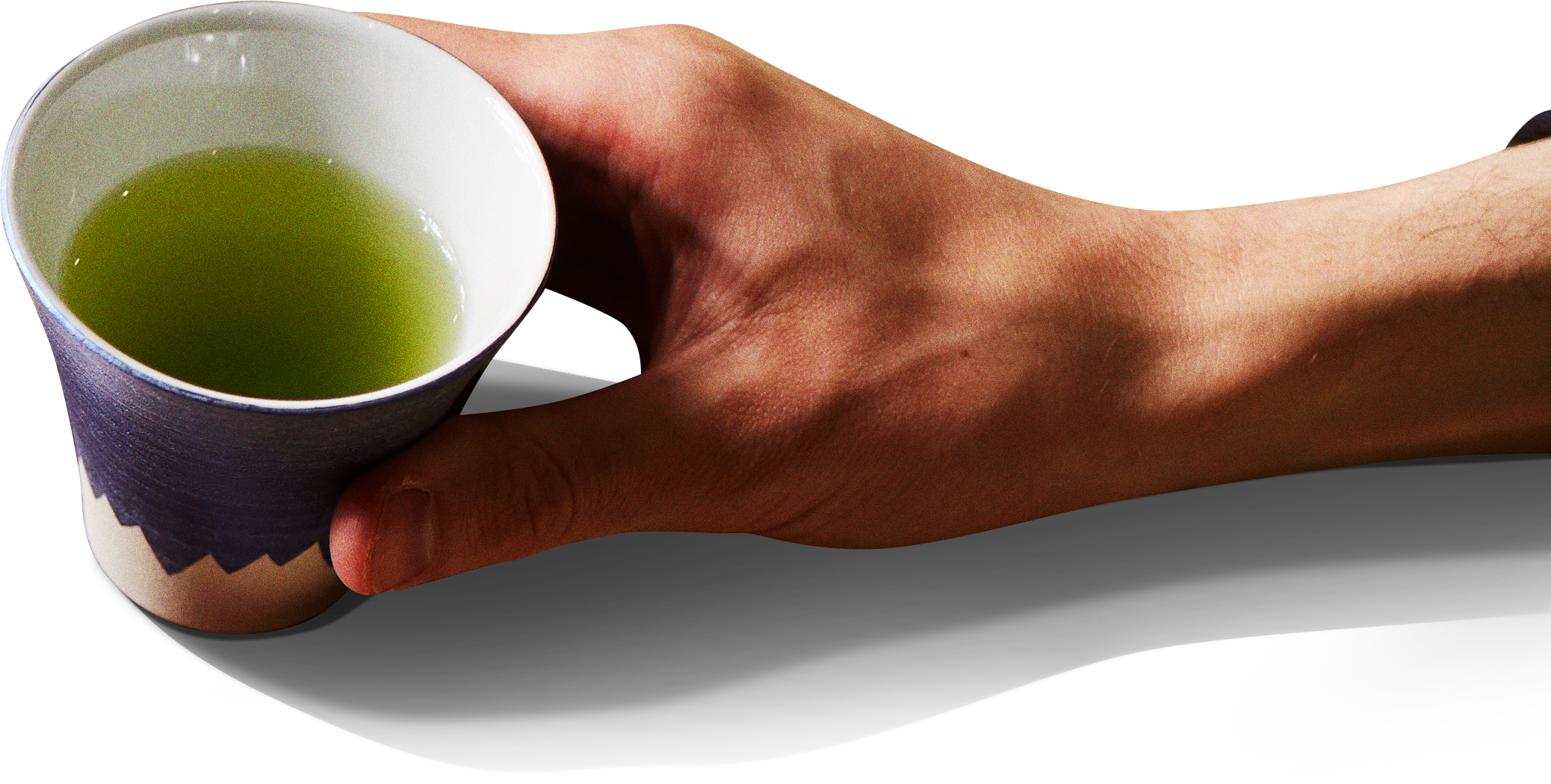 Hand holding a white and dark blue ceramic tea cup filled with bright green matcha tea, photographed against a white background