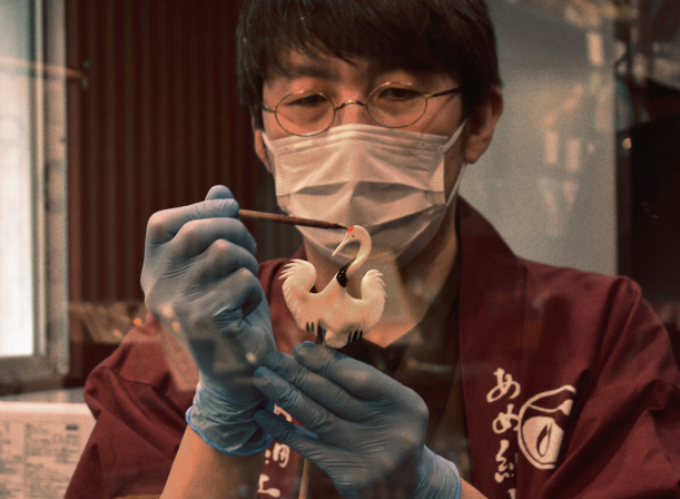 A Sakuraco Japan Snack Box beside and image of a man crafting authentic Japanese Candy.